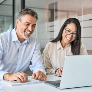 Happy smiling diverse colleagues executives team two professional managers looking at laptop pc having virtual meeting, watching webinar working together on online project sitting at office table.