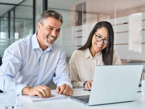 Happy smiling diverse colleagues executives team two professional managers looking at laptop pc having virtual meeting, watching webinar working together on online project sitting at office table.